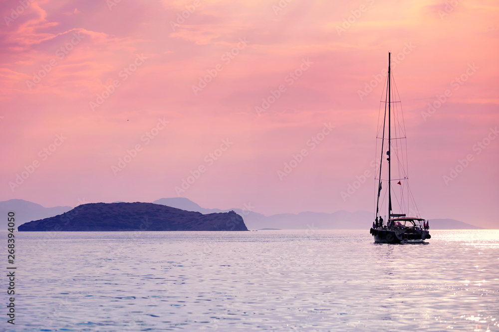 Sailboat anchored near an island over the calm sea at sunset colors