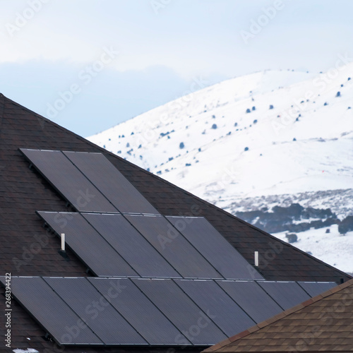 Square Solar panels installed on the dark roof of a home with snow in winter