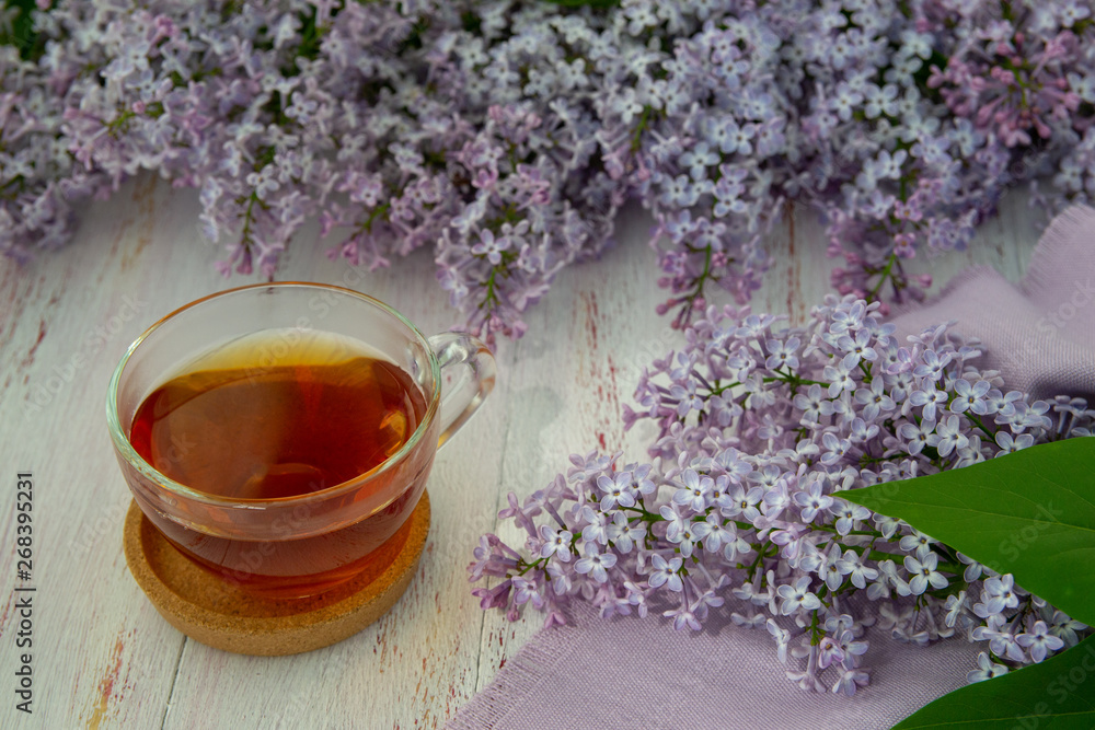 Spring flowers of lilac and leaves , a mug of tea on a wooden background. Decorative frame, top view. Spring flowers of lilac and leaves , a mug of tea on a wooden background. Decorative frame, top view.