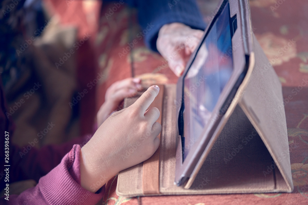 Obraz premium Photograph of the hands of a child and his grandmother using a tablet. Huelva, Spain