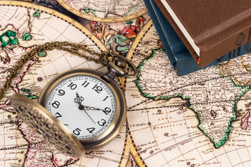 Vintage pocket watch clock on ancient map background with books