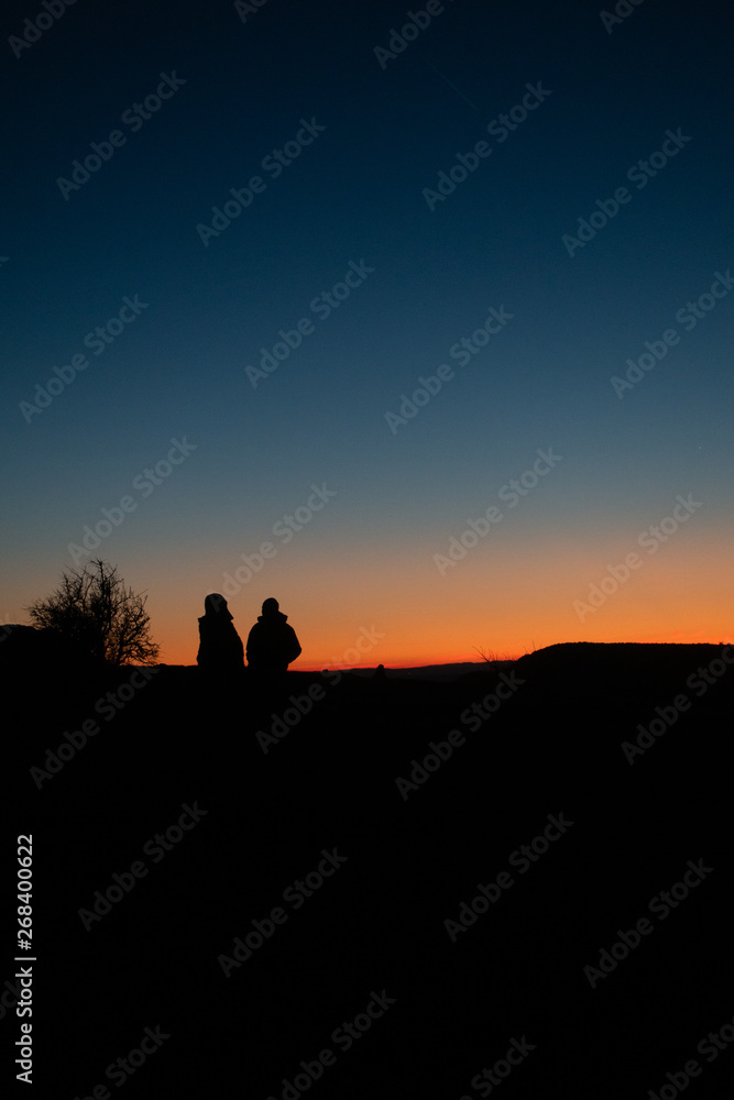 People sitting in dark sunset looking to horizon