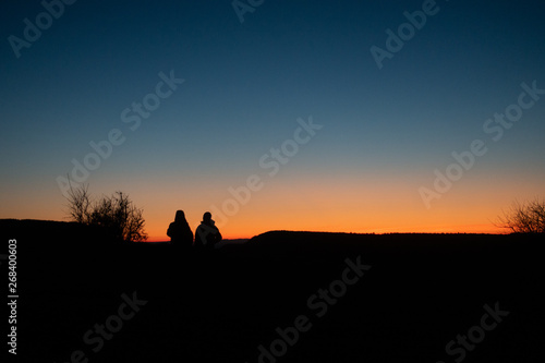 People sitting in dark sunset looking to horizon