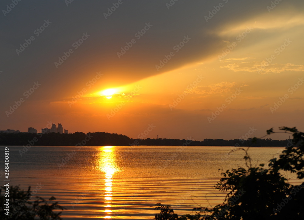 summer sunset over the river on the background of the city, the solar path on the water