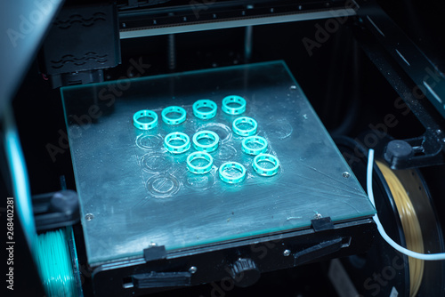 The 3D printer prints the many rings of the blue plastic. 3D printing of ABS or PLA plastic on a transparent glass platform.