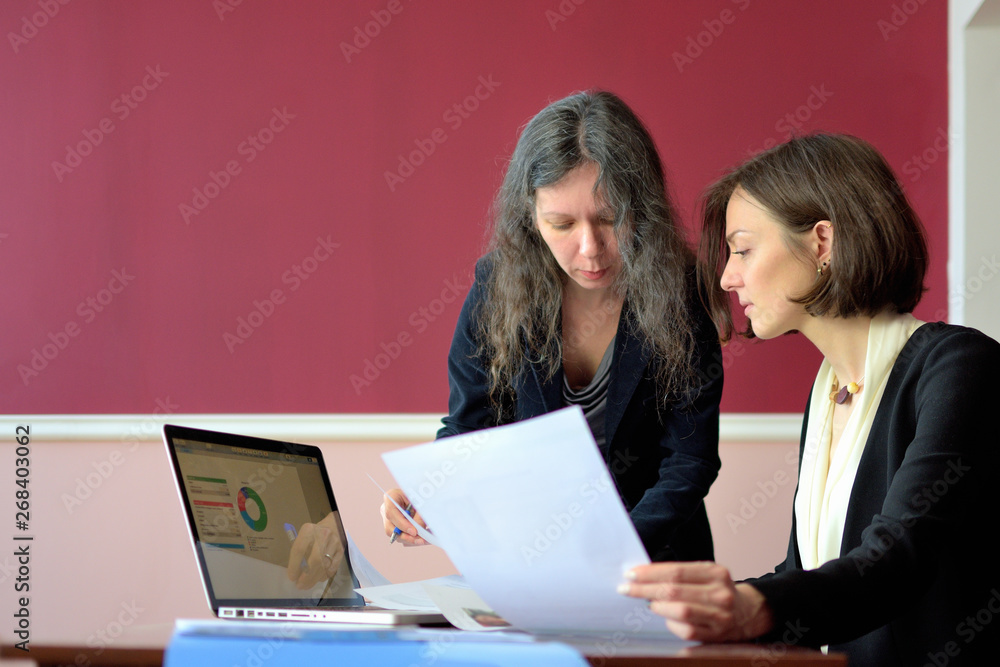 young smartly dressed lady helps another young lady to work with documents, fill forms and sign young smartly dressed lady helps another young lady to work with documents, fill forms and sign