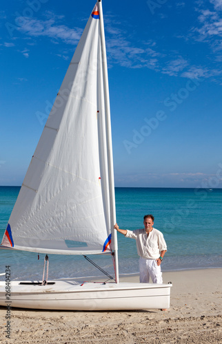 Cuba. A man on the blue sea next to a boat with a sail.. © Konstantin Kulikov