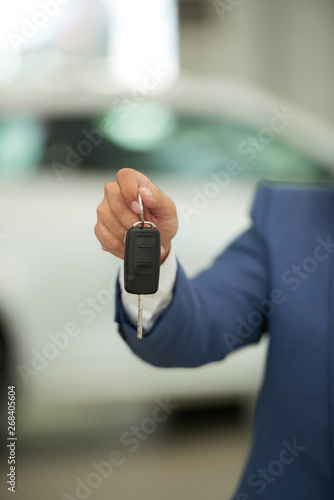 Close-up of man holding keys from new car, he buying or renting a new car in car showroom