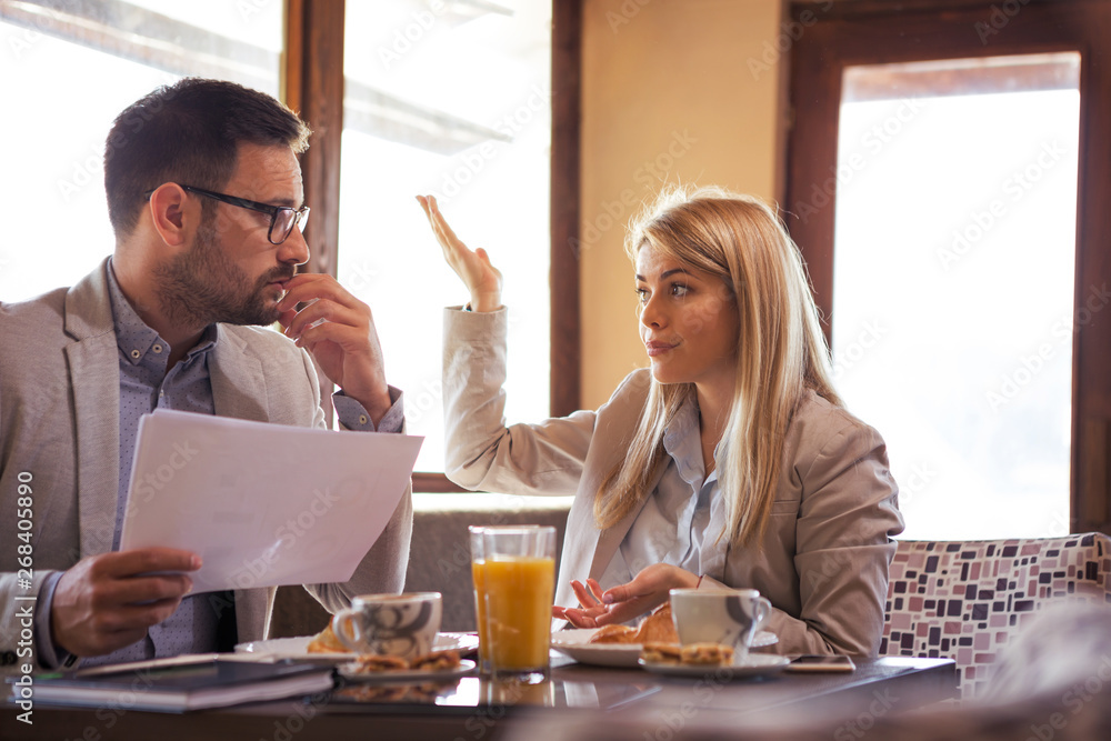 A beautiful young blonde boss explains to the manager what's wrong with his report while sitting and drinking coffee and juice A beautiful young blonde boss explains to the manager what's wrong with his report while sitting and drinking coffee and juice