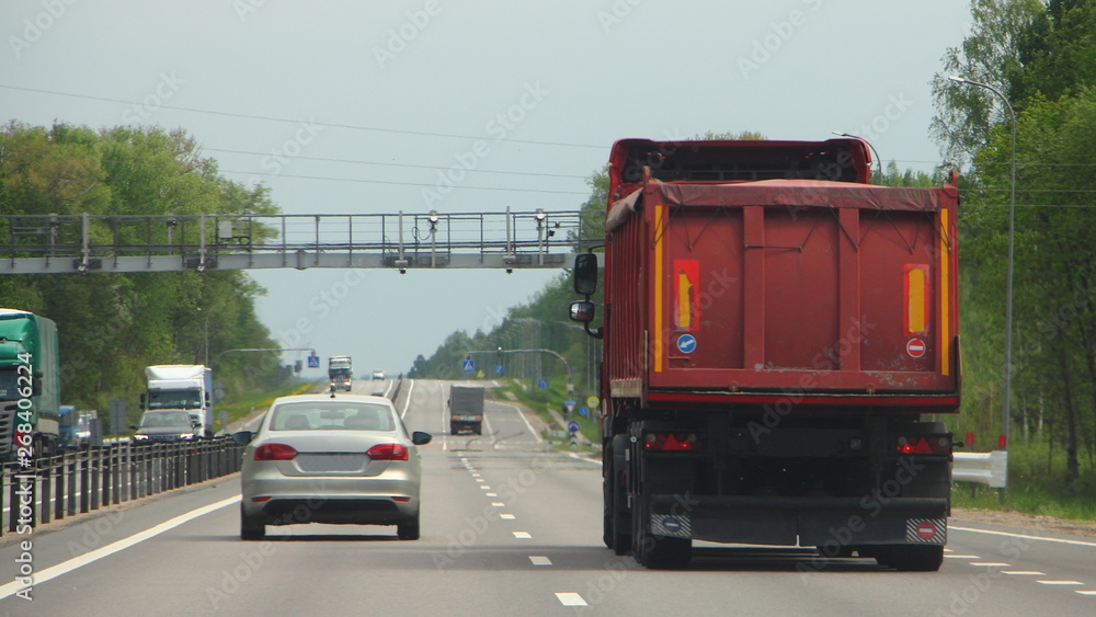 Red dump truck moving before speed control frame on asphalt road on summer day
