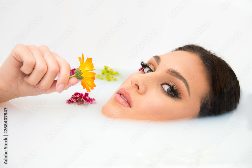attractive Caucasian model in milk bath with perfect teeth, face, skin and lips, and natural make up, beauty and spa concept with flowers and tropical leaves attractive Caucasian model in milk bath with perfect teeth, face, skin and lips, and natural make up, beauty and spa concept with flowers and tropical leaves