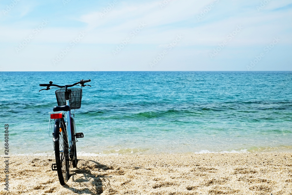 Fototapeta premium Feminine bicycle of comfort class with empty basket on the sandy beach of mediterranean sea. Blue cruiser bike on sunny day at sea shore with a lot of copy space for text.
