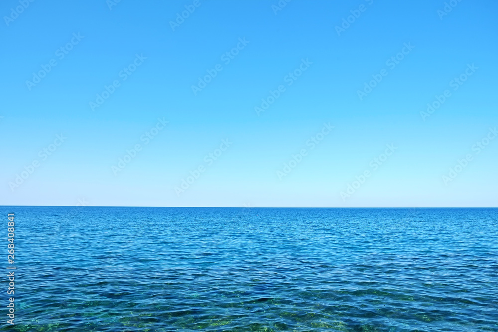 Obraz premium Beautiful seascape on sunny day with wind patterns on calm azure water and clear blue sky without clouds. Ocean view with horizon, background with a lot of copy space for text.
