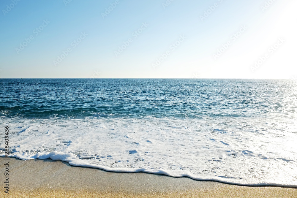 Top view shot of sea foam on sandy beach shore on sunny day. Ocean scenery with calm azure water and golden sand, a lot of copy space for text. Close up.