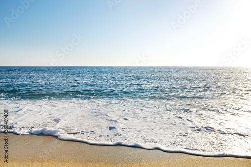 Top view shot of sea foam on sandy beach shore on sunny day. Ocean scenery with calm azure water and golden sand  a lot of copy space for text. Close up.
