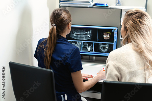 Female doctor shows the patient an x-ray image at display. Computer diagnostics dental tomography. Planning teeth treatment in modern dental clinic