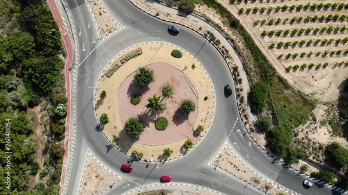 A roundabout planted with green trees on the Spanish national road N332 taken vertically from above with many vehicles in the sunshine.