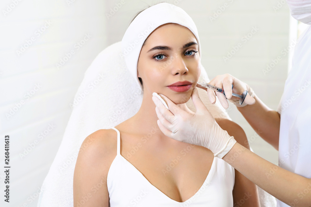 Lips injection close up. Syringe with filler for face contouring or augmentation. Cheerful young woman getting botox procedure. Beautician doctor standing near her. Healthcare cosmetology concept Lips injection close up. Syringe with filler for face contouring or augmentation. Cheerful young woman getting botox procedure. Beautician doctor standing near her. Healthcare cosmetology concept