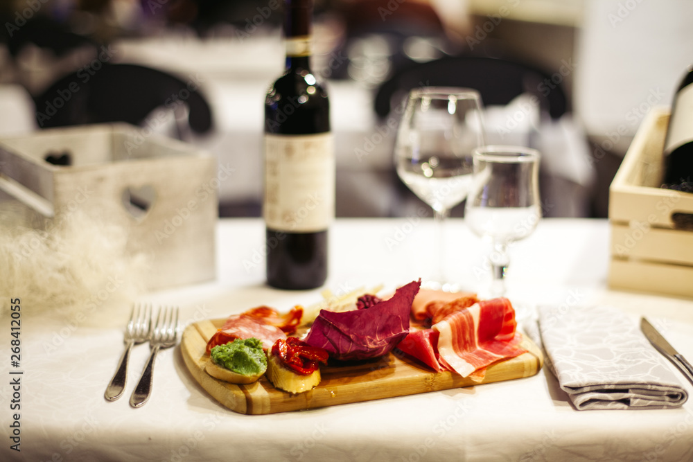 Table setting: white plates, rustic cloth with salami, cheese, vine, ham and wine bottle