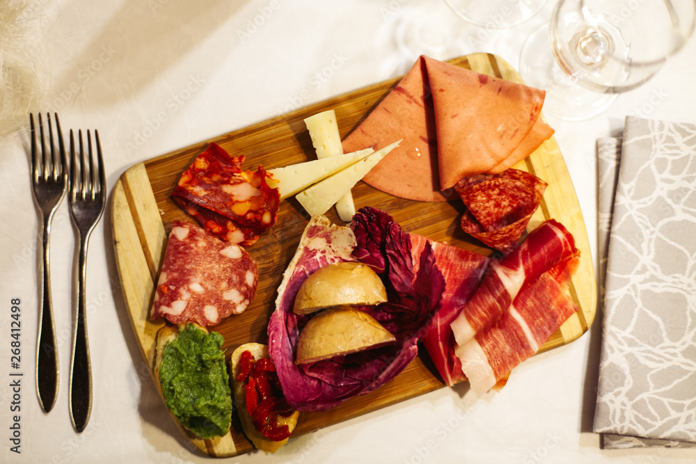 Table setting: white plates, rustic cloth with salami, cheese, vine, ham and wine bottle Table setting: white plates, rustic cloth with salami, cheese, vine, ham and wine bottle