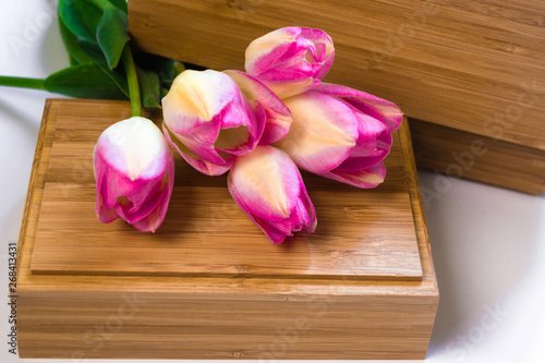 A bouquet of flowers on a white background with wooden crusts. Purple tulips on a wooden box. Place for text. Top view.