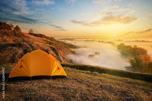 Orange tent in canyon over misty river at sunset