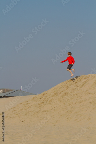 Blond boy in red sweater having fun on sand dunes in Holland