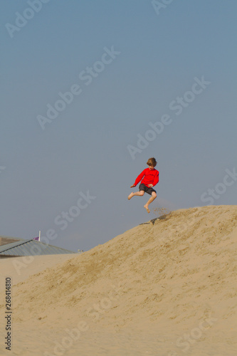Blond boy in red sweater having fun on sand dunes in Holland