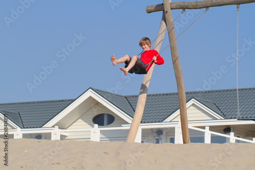 Blond boy in red sweater having fun on sand dunes in Holland