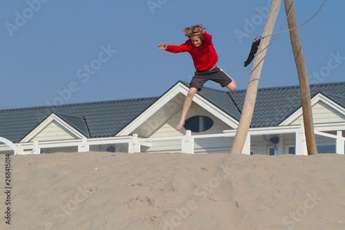 Blond boy in red sweater having fun on sand dunes in Holland