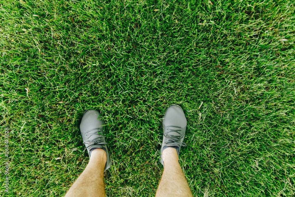 Male feet in running shoes standing on the grass, above view