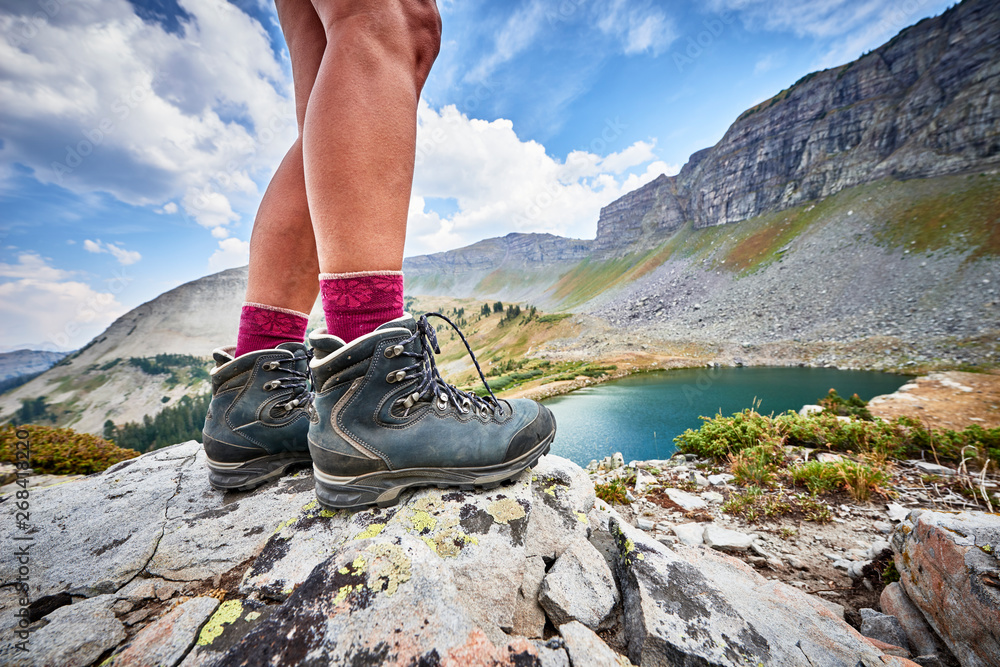 a young woman wearing hiking boots and trekking around an alpine mountain lake - obrazy, fototapety, plakaty 