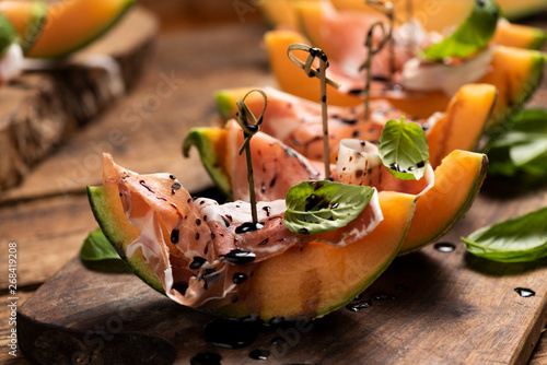 Sliced melon with ham and basil leaves, served on a wood chopping board photo