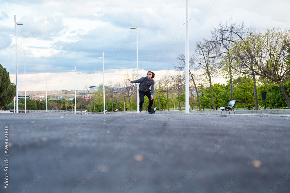 From below young cool male in sportswear riding on roller skates very fast on road in park