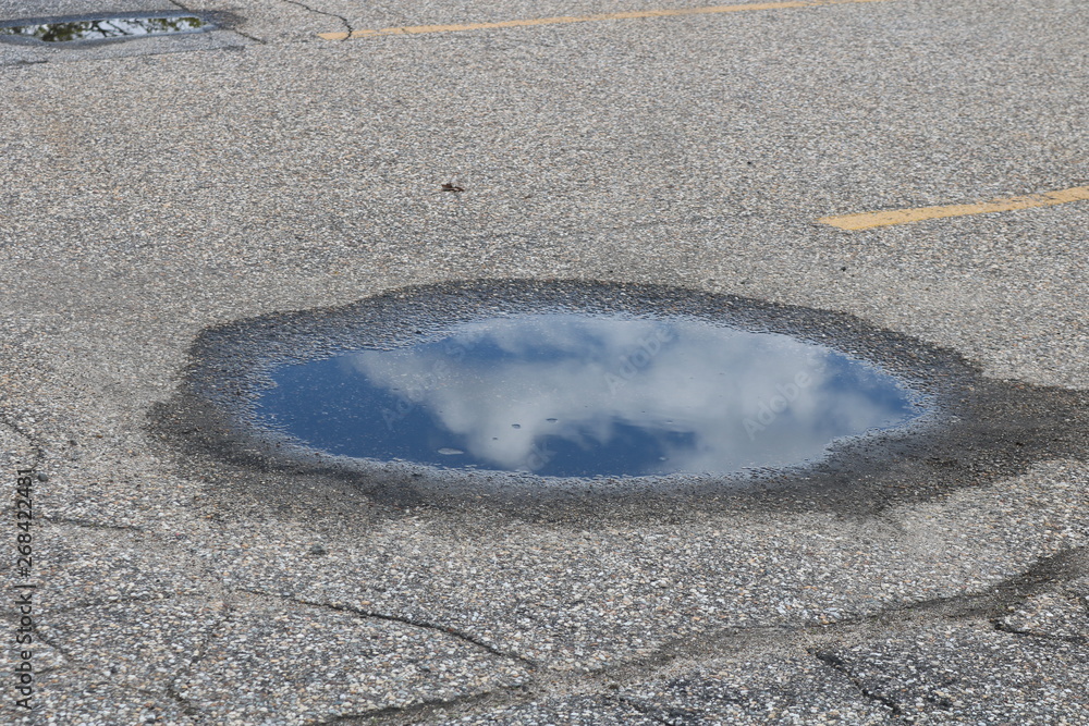 Blue sky and clouds reflected in water puddle on street pavement Blue sky and clouds reflected in water puddle on street pavement