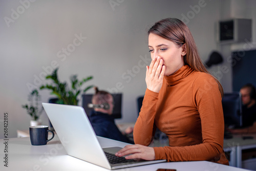 Young woman yawning in the office, looking tired and exhausted.