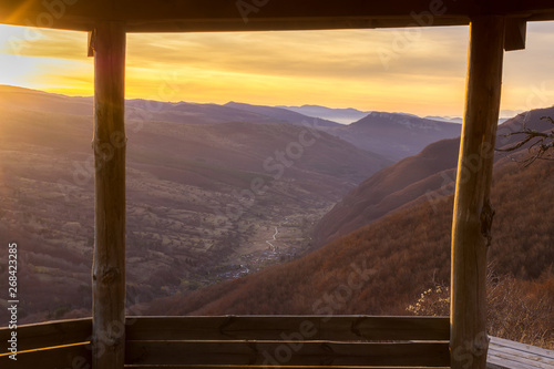 Framed view through the wooden summer house on a valley of village Dojkinci and beautiful sunrise in the mountains photo