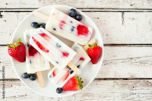 Healthy strawberry blueberry yogurt ice pops on a plate, top view against a white wood background photo