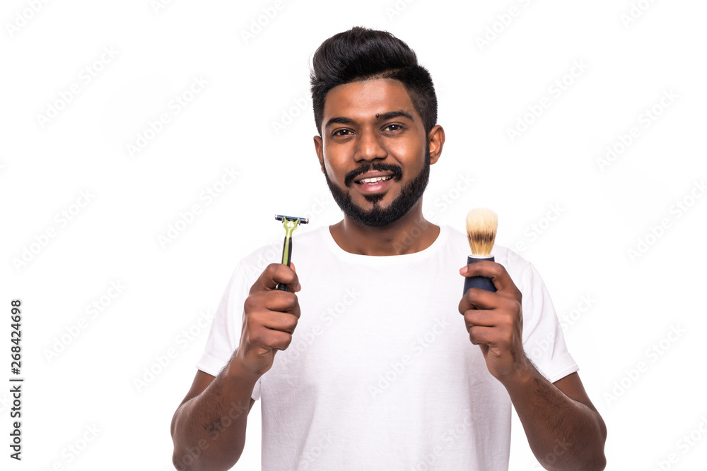 Handsome young indian man standing with razor in hand on white background. Men care concept. Get hurt while shaving. Handsome young indian man standing with razor in hand on white background. Men care concept. Get hurt while shaving.
