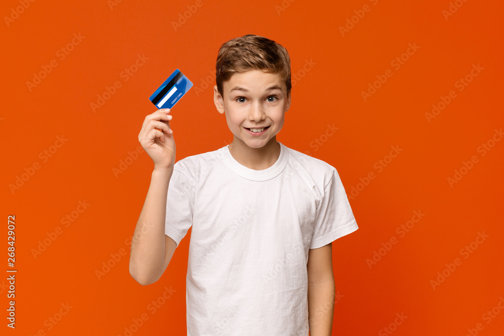 Cute boy holding credit card, orange studio background Cute boy holding credit card, orange studio background