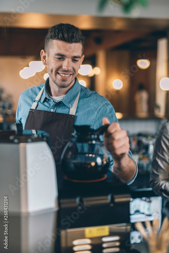 Close up of smiling barista putting coffee jug on the coffee machine
