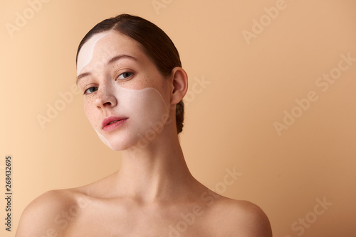 Charming young woman with mask on her face standing against beige background