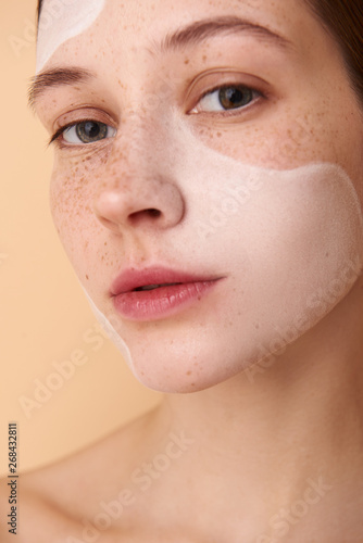 Attractive girl with white mask on face standing against beige background