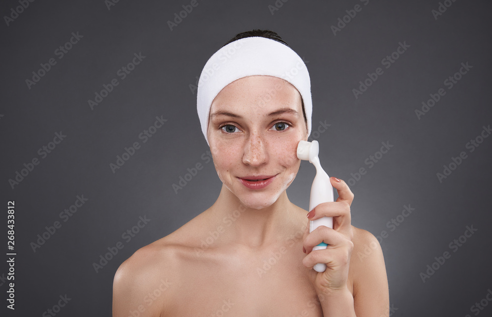Smiling girl in white headband using pore cleansing brush after bath Smiling girl in white headband using pore cleansing brush after bath