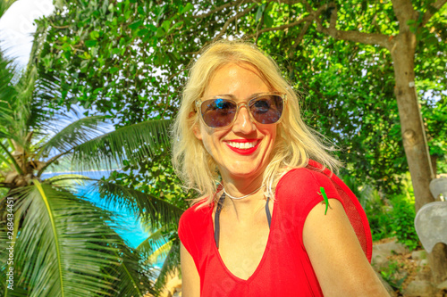 A cute Phelsuma sundbergi called La Digue day gecko on arm of a smiling tourist woman on vacation at Seychelles. Happy caucasian female enjoys with lizard, wildlife of La Digue. photo