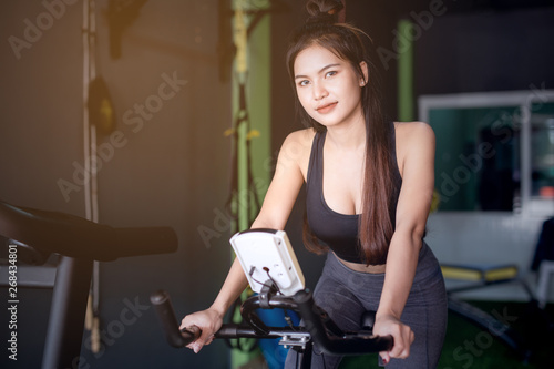 Beautiful, sexy Asian woman smiling while exercising with a bike in the gym