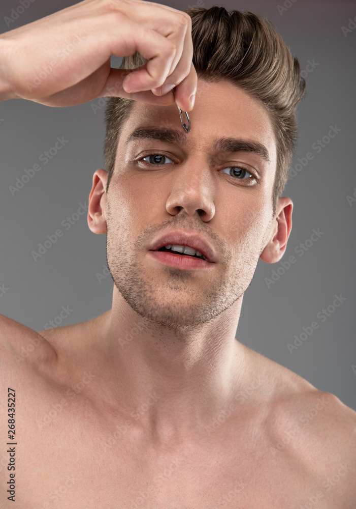 Obraz premium Handsome young man plucking eyebrows with tweezers