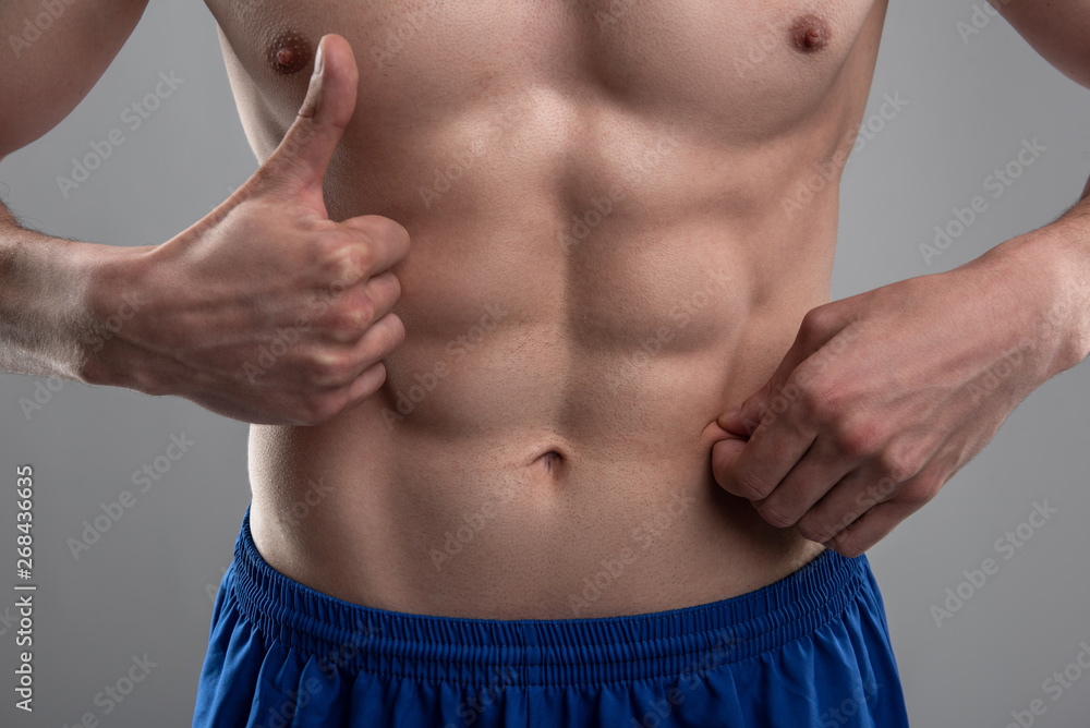Young man demonstrating his six-pack abs and showing thumbs up