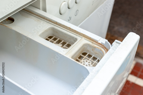 Dirty moldy washing machine detergent and fabric conditioner dispenser drawer compartment close up. Mold, rust and limescale in washing machine tray. Home appliances periodic maintenance