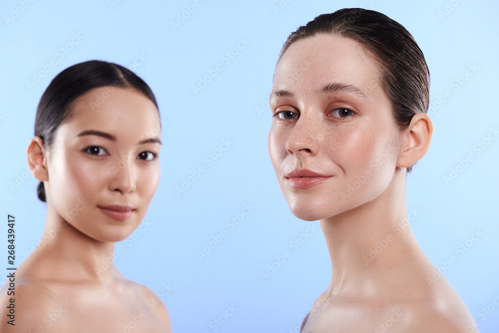 Waist up of charming interracial women situating against blue background Waist up of charming interracial women situating against blue background